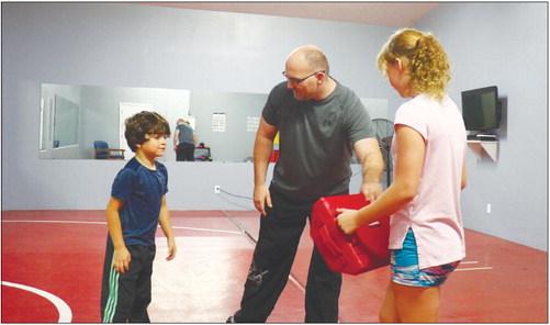 BRANDON SCHMIDT leads his son, Lucian, 7, in a warmup for training at D-D Gym in St. Paul last Wednesday night. Schmidt’s daughter, Bentley, 11, holds the strike pad. Photo by Michael Rother