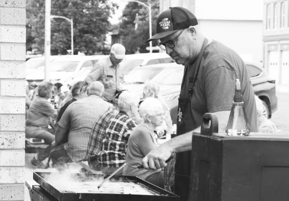 CITIZENS BANK AND TRUST CO. President/Trust Officer Jeff Varney grills up burgers in front of the bank along Howard Avenue in St. Paul on Tuesday. A large crowd turned out for the bank’s Community BBQ, with many staying to converse and eat along main street.