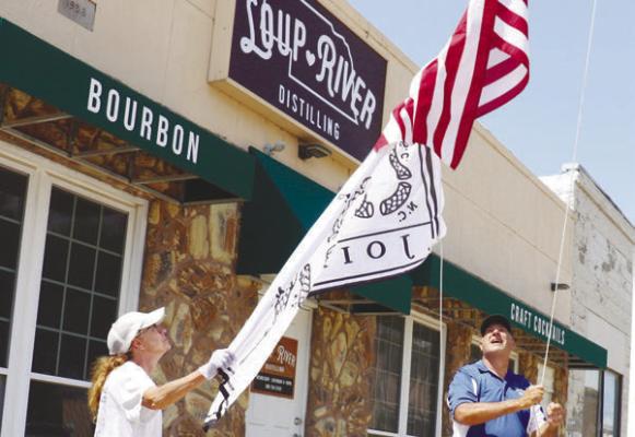 ERIC MONTEMAGNI, with the help of his wife, Maria, works to hoist a pair of flags, including a flag modeled on Ben Franklin’s “Join, or Die” woodcut, outside of Loup River Distilling last week. Photo by Michael Rother