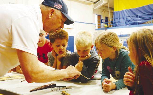CONSERVATION BLUEPRINT FOUNDER AND PRESIDENT PETE BERTHELSEN shows a group St. Paul second graders how insects make use of cavities in prairie plants—as well as the bamboo stakes Conservation Blueprint employees use to mark the locations of plant populations for harvest— as part of their life cycles during the organization’s visit to the St. Paul Public Schools elementary gymnasium last Thursday. Photo by Michael Rother