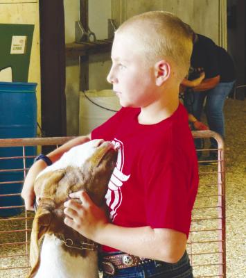 GUNNER SPIEHS, the son of Jason and Ginney Spiehs, waits patiently to sell his 4-H Supreme Market Goat during last Wednesday’s Howard County Fair Premium Auction. The fair completed its five-day run outside of St. Paul last week, with the premium auction capping off the 4-H and FFA activities. Photo by Michael Happ