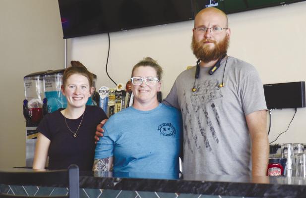 BEHIND THE BAR in The Den’s newly renovated west side are Alyssa Gdanitz, a server, and Jewell and Isaac Howell, owners. Photo by Michael Rother
