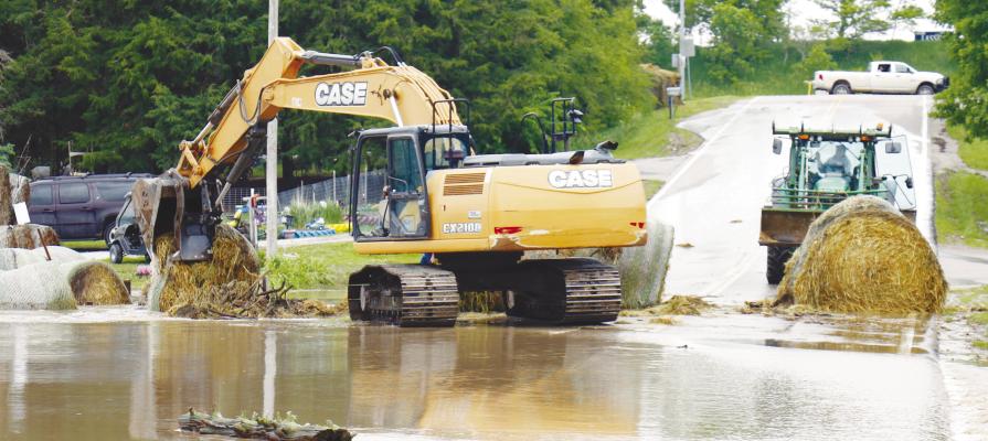 WITH THE WATER LEVEL RECEDING along Lander Avenue on Thursday afternoon, work to remove bales of hay from the floodwaters on the north side of Farwell begins. Heavy rains inundated portions of western Howard County with water last week. Photo by Michael Rother