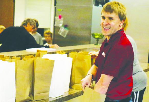 TYLER EBERLE with Archer Credit Union assembles sack lunches during last Thursday’s Lunch Bunch at the Sts. Peter and Paul Parish Life Center. Photo by Michael Rother