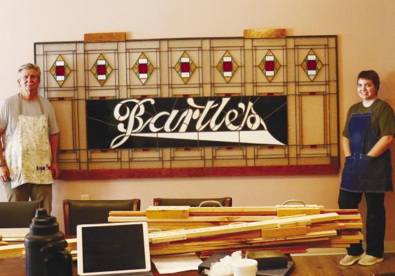 THE HISTORIC BARTLE’S STORE SIGN was recently restored and returned to St. Paul last week. Artist Ken Eldridge, and his apprentice, Becca Robertson, are pictured next to the sign, which hangs in the exhibit hall at the Howard County Historical Village. Photo by Haley Spotanski