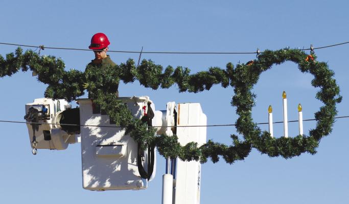 CREWS with the City of St. Paul were busy getting the Howard County community decked out for the holidays last Monday afternoon. Above, City of St. Paul Employee Jarod Greenough works to hang garland over Howard Avenue near the railroad tracks. Photo by Michael Rother
