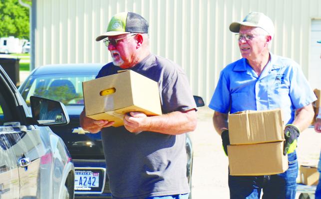 FOOD PANTRY VOLUNTEERS James Zimbelman and Don Gorecki help carry boxes to vehicles during last Tuesday’s produce distribution event. Photo by Michael Rother