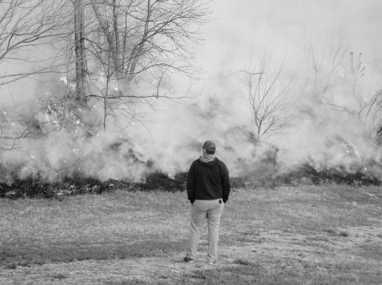 WOLBACH VOLUNTEER FIREFIGHTER Matt Steenson watches the burn on the east side of Memorial Field in Wolbach on Monday night. The local department conducted a pair of burns in town that evening. (Michael Rother)