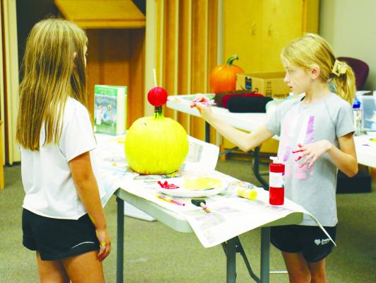 JAMISYN FOUSEK lends Rowynn Gorecki a hand painting her pumpkin last month as a part of the St. Paul Library’s Literary Pumpkin Project. Photos by Michael Rother