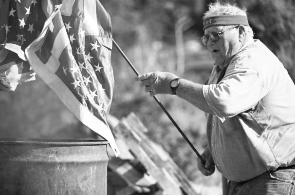 THE CARL MOGENSEN AMERICAN LEGION POST 119 of St. Paul retired more than 1,000 flags during a Flag Day retirement ceremony in St. Paul on Saturday. Above, Chuck Schmidt places a tattered flag in one of the burn barrels. Photo by Michael Happ