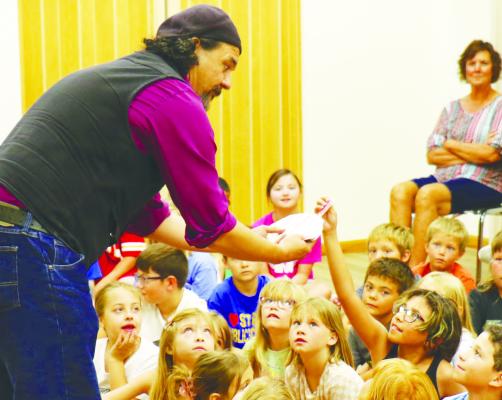 ISABELLA HERNANDEZ draws a card from Adam White’s deck during the St. Paul Library’s Summer Reading Magic Show last Tuesday. Photos by Michael Rother