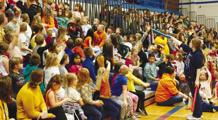EDGERTON EDUCATOR NICOLE HAULIK points towards an eager volunteer in the crowd at St. Paul Elementary during Edgerton on the Move’s Good Vibrations all school assembly last Wednesday morning. The sound-based assembly had been one of several events brought to the district by Edgerton last week. Photo by Michael Rother