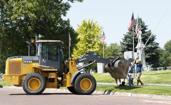 CITY UTILITIES SUPERINTENDENT Matt Helzer drives a loader, using a chain affixed to its bucket to pull the bent flagpoles in front of the Howard County Courthouse while others aid in removing the same. The group made quick work of removing the flagpoles last Thursday. (Michael Rother)
