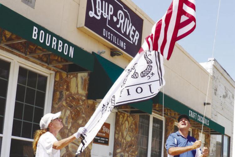 ERIC MONTEMAGNI, with the help of his wife, Maria, works to hoist a pair of flags, including a flag modeled on Ben Franklin’s “Join, or Die” woodcut, outside of Loup River Distilling last week. Photo by Michael Rother