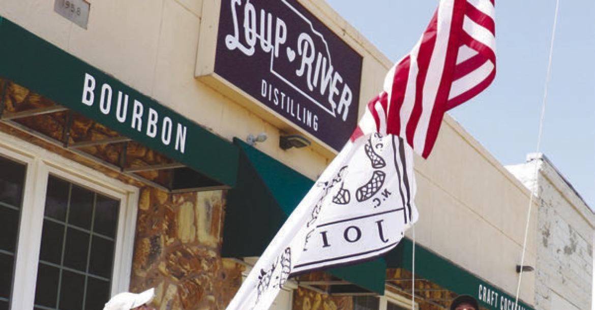 ERIC MONTEMAGNI, with the help of his wife, Maria, works to hoist a pair of flags, including a flag modeled on Ben Franklin’s “Join, or Die” woodcut, outside of Loup River Distilling last week. Photo by Michael Rother