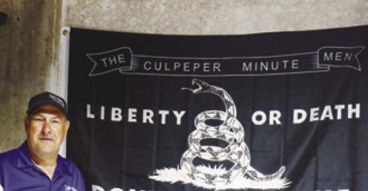ERIC MONTEMAGNI stands in front of a banner for the Culpeper Minutemen, a militia group from the revolutionary period, inside Loup River Distilling last week.